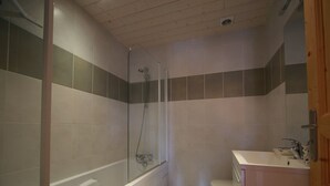 Ett badrum med en dusch som är avskärmad med glasväggar, ett vitt badkar, en toalett och ett handfat med en spegel.