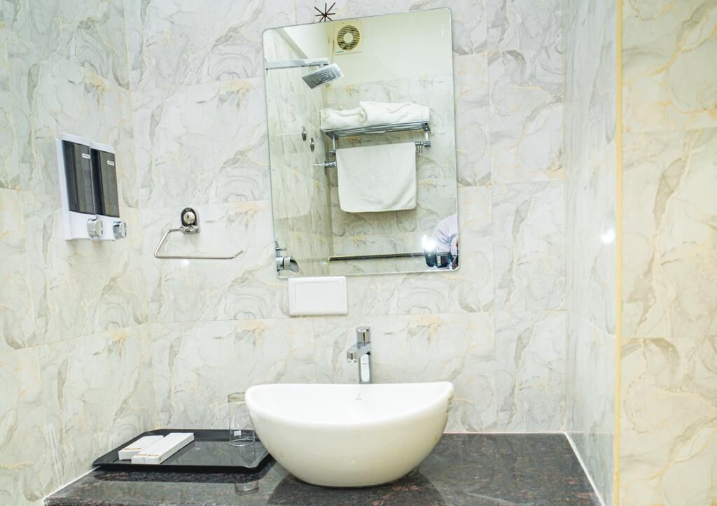 Un baño con pared de mármol, un lavamanos blanco, un espejo y un perchero para toallas.
