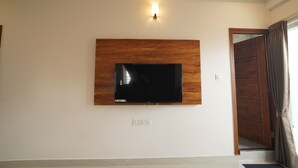 A room with a mounted TV on a wooden panel, a light switch, and a door with a curtain. - The Auberge - Boutique Hotel (Bengaluru)