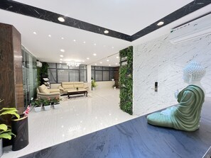 Een moderne lobby met een marmeren receptiebalie, een beige bank en een Boeddhabeeld.