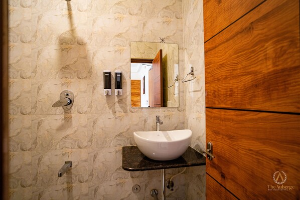 A bathroom with a marble wall, a wooden door, a white sink, and a mirror.