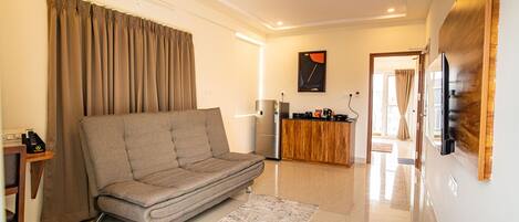 A modern living room with a sofa, a coffee table, a TV, and a kitchen area in the background.