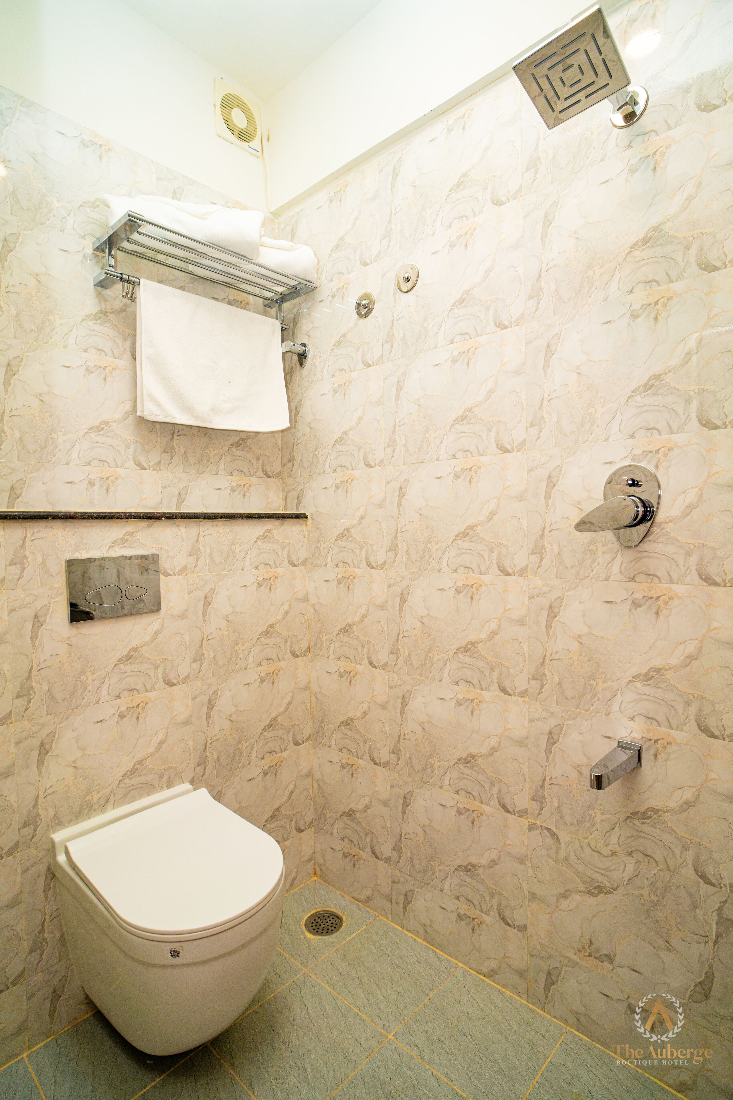 A bathroom with a marble-patterned wall, a toilet, a towel rack, and a showerhead.