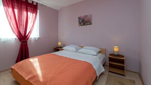 A bedroom with a bed, two bedside tables with lamps, a window with red curtains, and a wall-mounted picture. - Anto - 3 bedroom apartment in Trogir (Trogir)