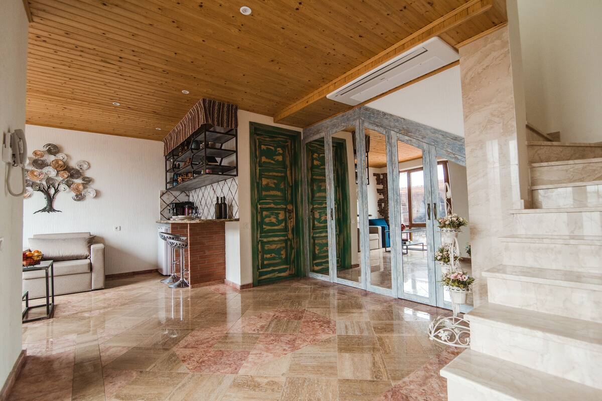 A spacious living area with a wooden ceiling, a kitchen area, and a staircase leading to an upper floor.
