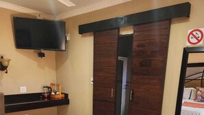 A hotel room with a bed, a TV mounted on the wall, a wooden wardrobe, and a mirror on the wall. - Suits bar restaurant and guesthouse (Merafong City)