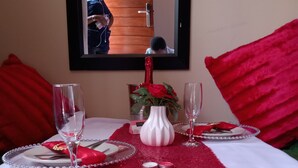 A dining table set with red and white tablecloth, two wine glasses, a white vase with red roses, and a mirror on the wall. - Suits bar restaurant and guesthouse (Merafong City)