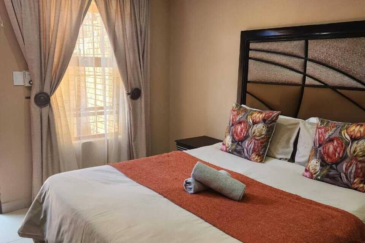 A neatly made bed with a red blanket, floral pillows, and a headboard with a geometric pattern.