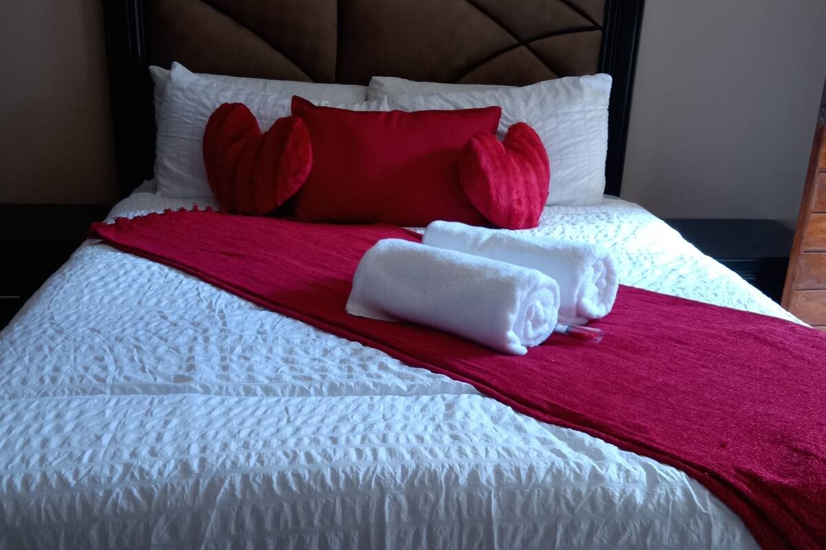 A neatly made bed with white bedding, red pillows, and a red throw blanket.