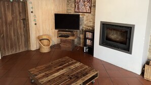 Una sala de estar rústica con una mesa de madera, chimenea, televisor y pared de piedra.