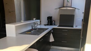 Una cocina moderna con encimera blanca, lavaplatos de acero inoxidable y armarios negros. Hay un reloj en la pared y una cafetera sobre la encimera.