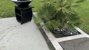 Un patio con una parrilla exterior negra y una planta de palmera.