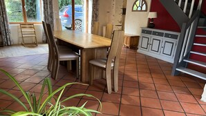 Un comedor con mesa y sillas de madera, una planta en maceta y una cocina con armarios y una escalera.