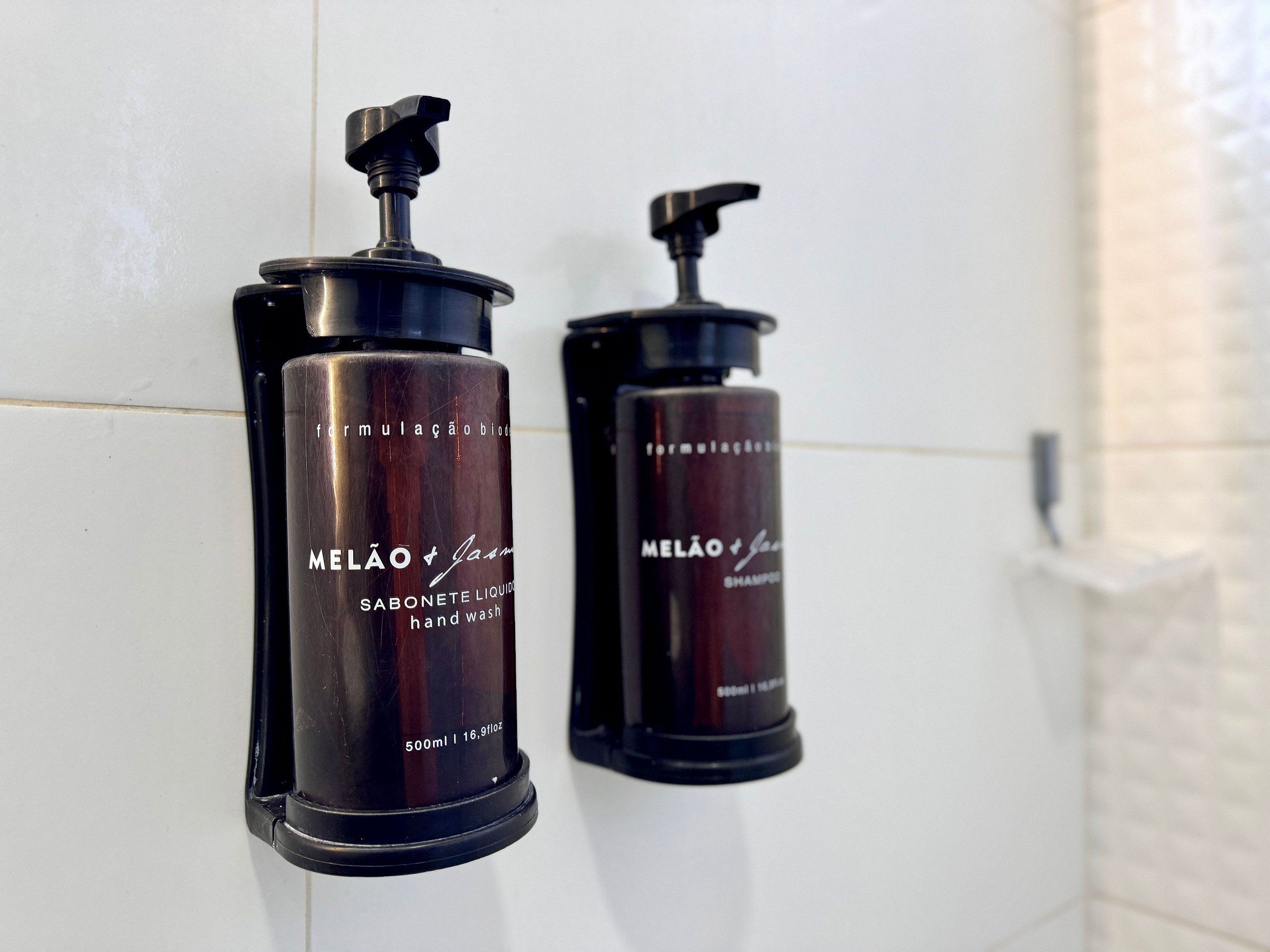 Two black hand soap dispensers labeled "MELÃO" on a white tiled wall.