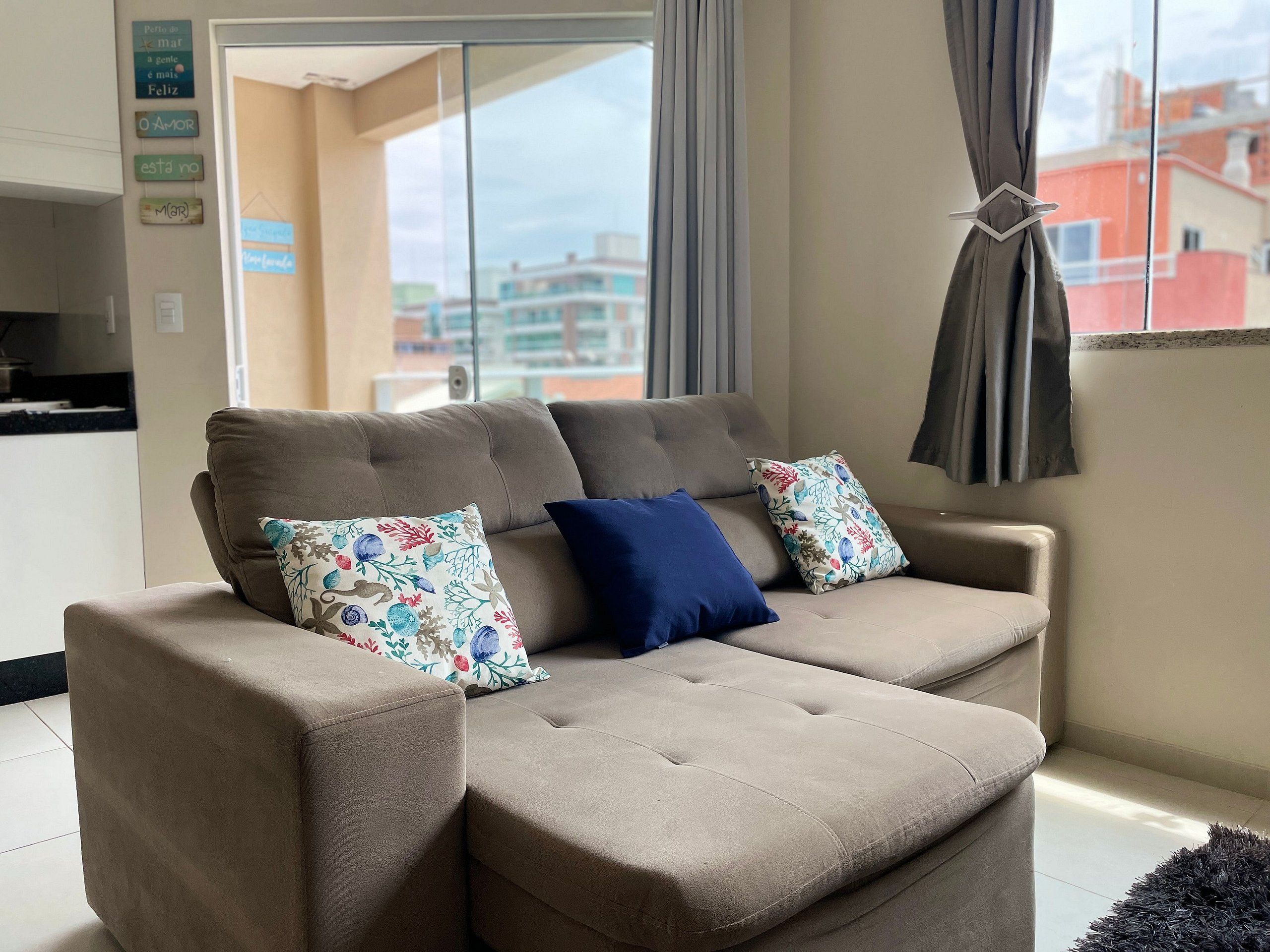 A beige sectional sofa with floral and solid blue cushions in a room with a view of buildings through a large window.