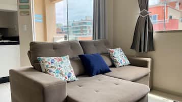 A beige sectional sofa with floral and solid blue cushions in a room with a view of buildings through a large window.