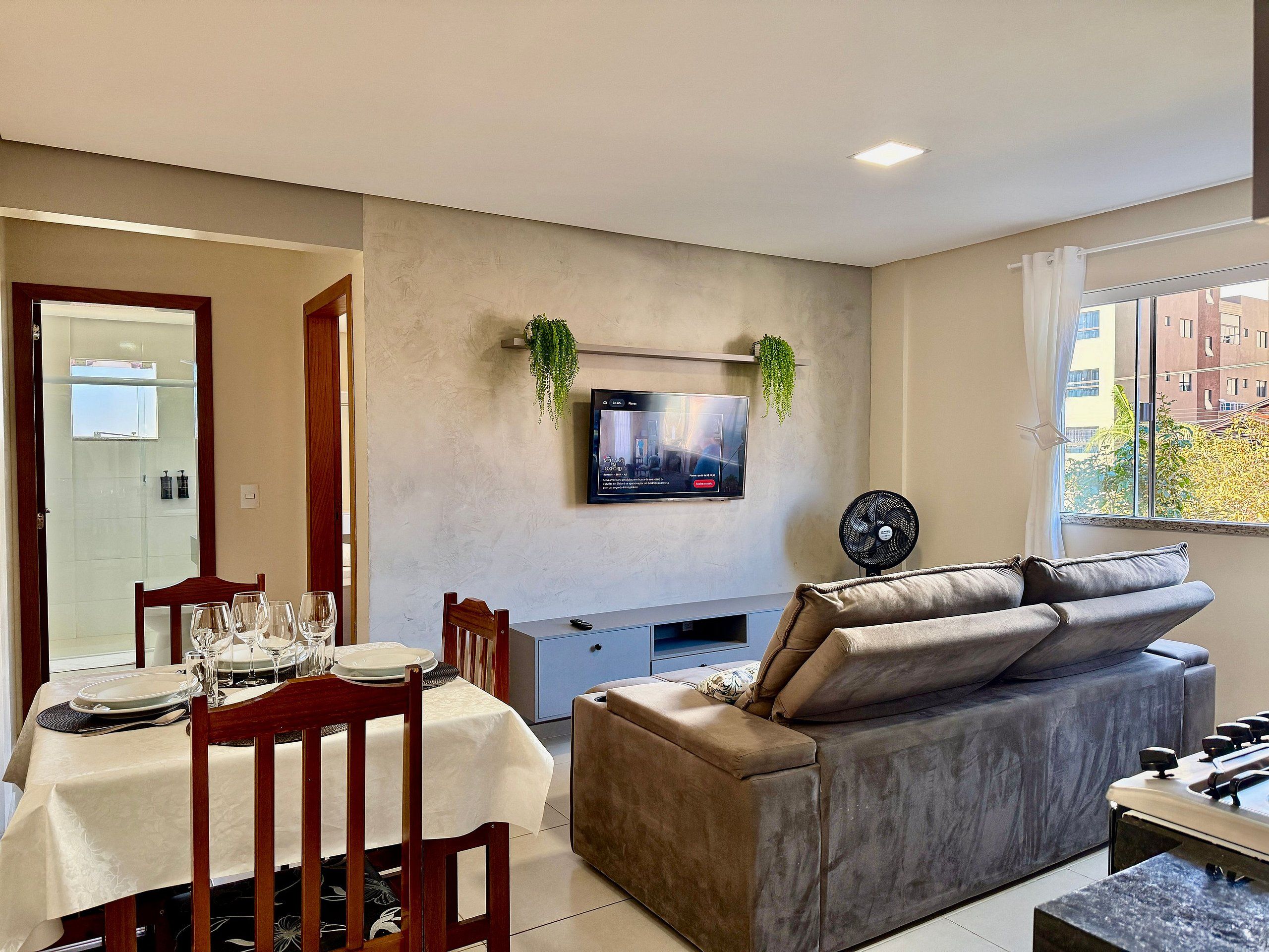 A modern living room with a dining area, a flat-screen TV mounted on the wall, a sofa, and a foosball table.