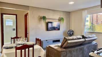 Un salon moderne comprenant un coin repas, un téléviseur à écran plat fixé au mur, un canapé et une table de baby-foot.