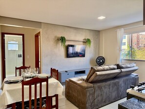 A modern living room with a dining area, a flat-screen TV mounted on the wall, a sofa, and a foosball table. - Maria Julia (Bombinhas)