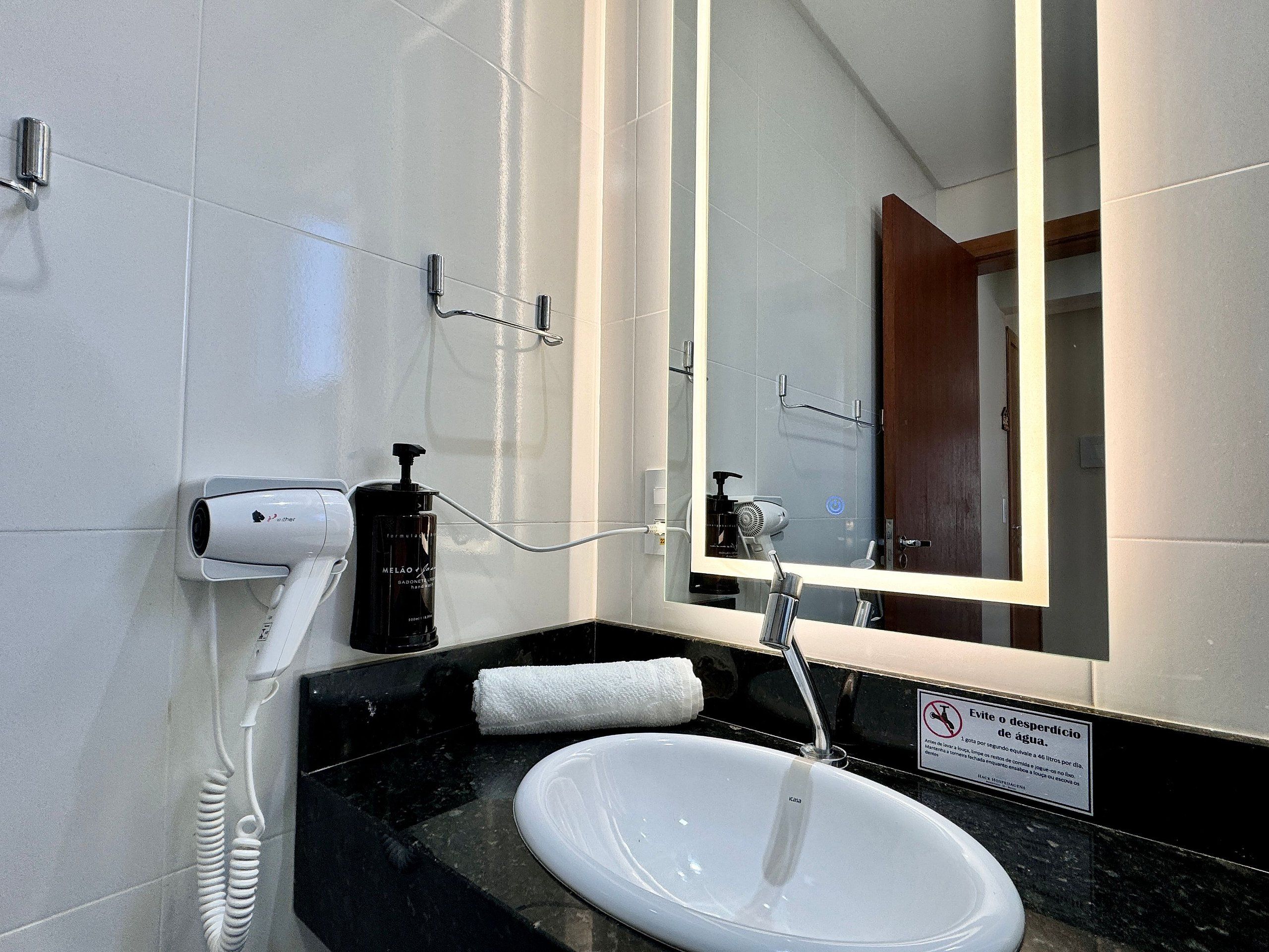 A bathroom with a white sink, a mirror, a hairdryer, and a towel.