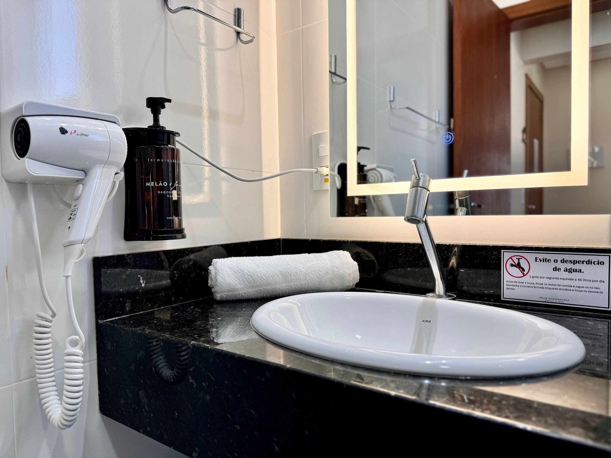 Een badkamer met een wit wastafel, een spiegel, een haardroger en een zeepdispenser.