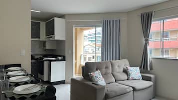 A modern living room with a sofa, a dining table set with plates and glasses, and a kitchen in the background.
