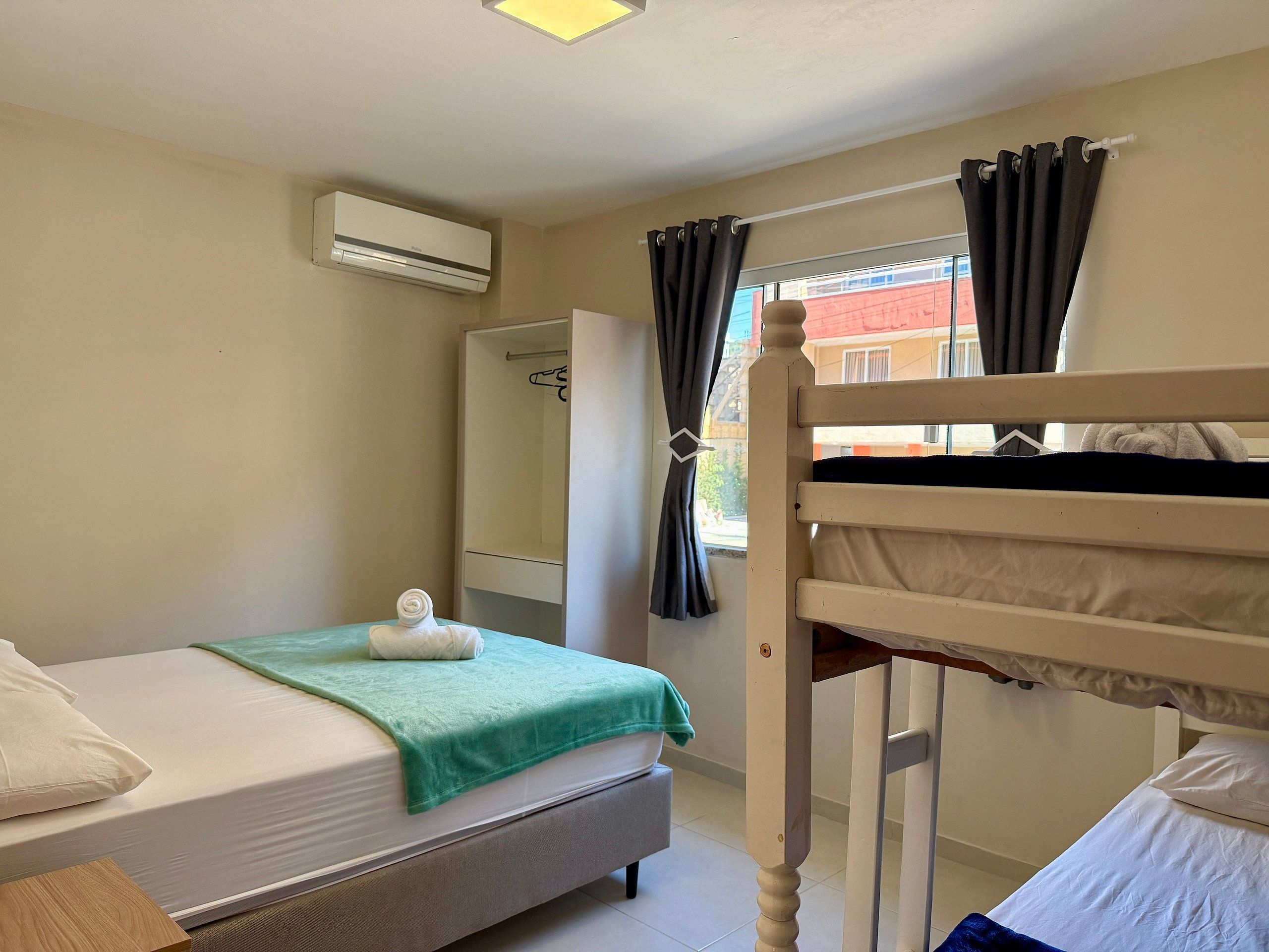 A bedroom with a bunk bed, a single bed, a wardrobe, and an air conditioning unit.