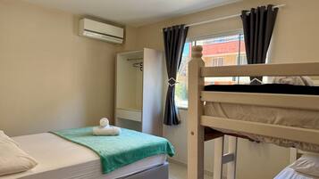 A bedroom with a bunk bed, a single bed, a wardrobe, and an air conditioning unit.