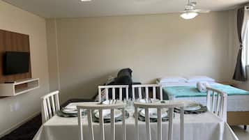 A hotel room with a bed, a dining table set for two, a TV mounted on the wall, and a ceiling fan.
