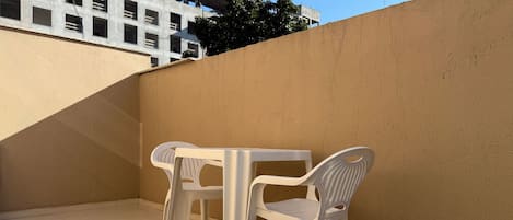 A small outdoor patio area with a white table and two white plastic chairs, a tiled floor, and a beige wall.