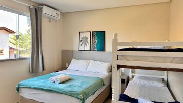 A hotel room with a bed, a bunk bed, a window with curtains, an air conditioning unit, and a framed picture on the wall.