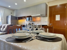 Uma mesa de jantar posta com pratos, copos e talheres, com uma cozinha ao fundo.