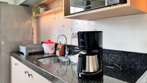 A kitchen with a coffee maker on the counter, a microwave above, and a sink with a faucet. - Maria Julia (Bombinhas)