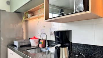 A kitchen with a coffee maker on the counter, a microwave above, and a sink with a faucet.