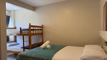 A single bed with a green blanket and white pillows, a wooden bunk bed in the background, and a mirror on the wall.
