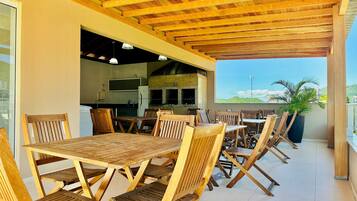 Un área de comedor al aire libre con mesas y sillas de madera, una cocina al fondo y vistas del paisaje.