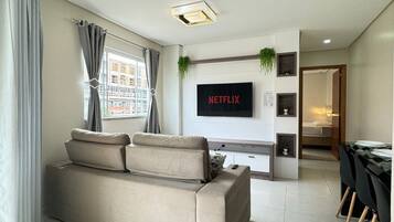 Una sala de estar moderna con un sofá, un televisor montado en la pared y un comedor con mesa y sillas.