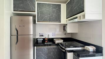 Cozinha compacta com geladeira, fogão, micro-ondas e armários com acabamento que imita mármore.