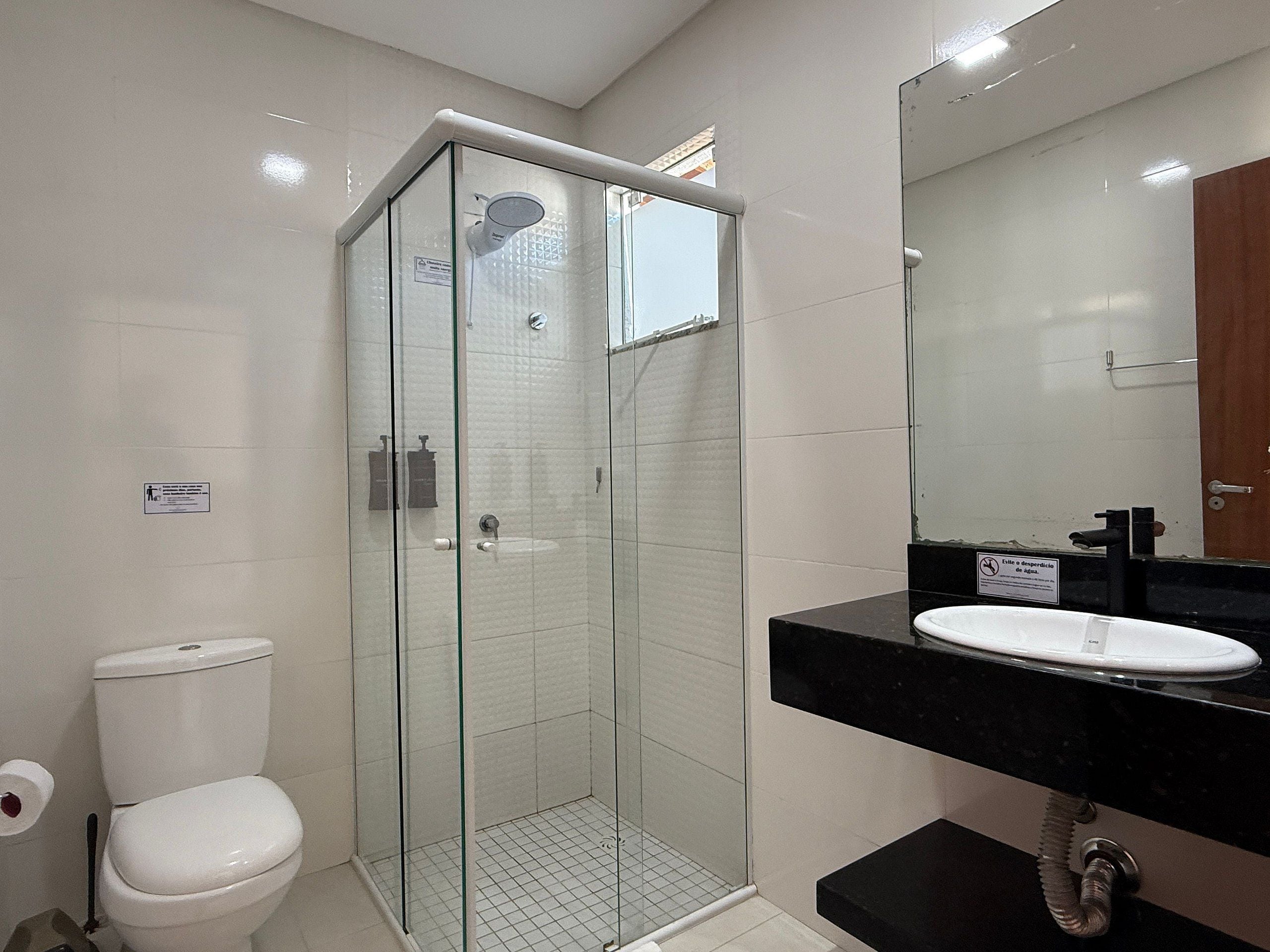 A modern bathroom with a glass-enclosed shower, a white toilet, and a black sink with a mirror above it.