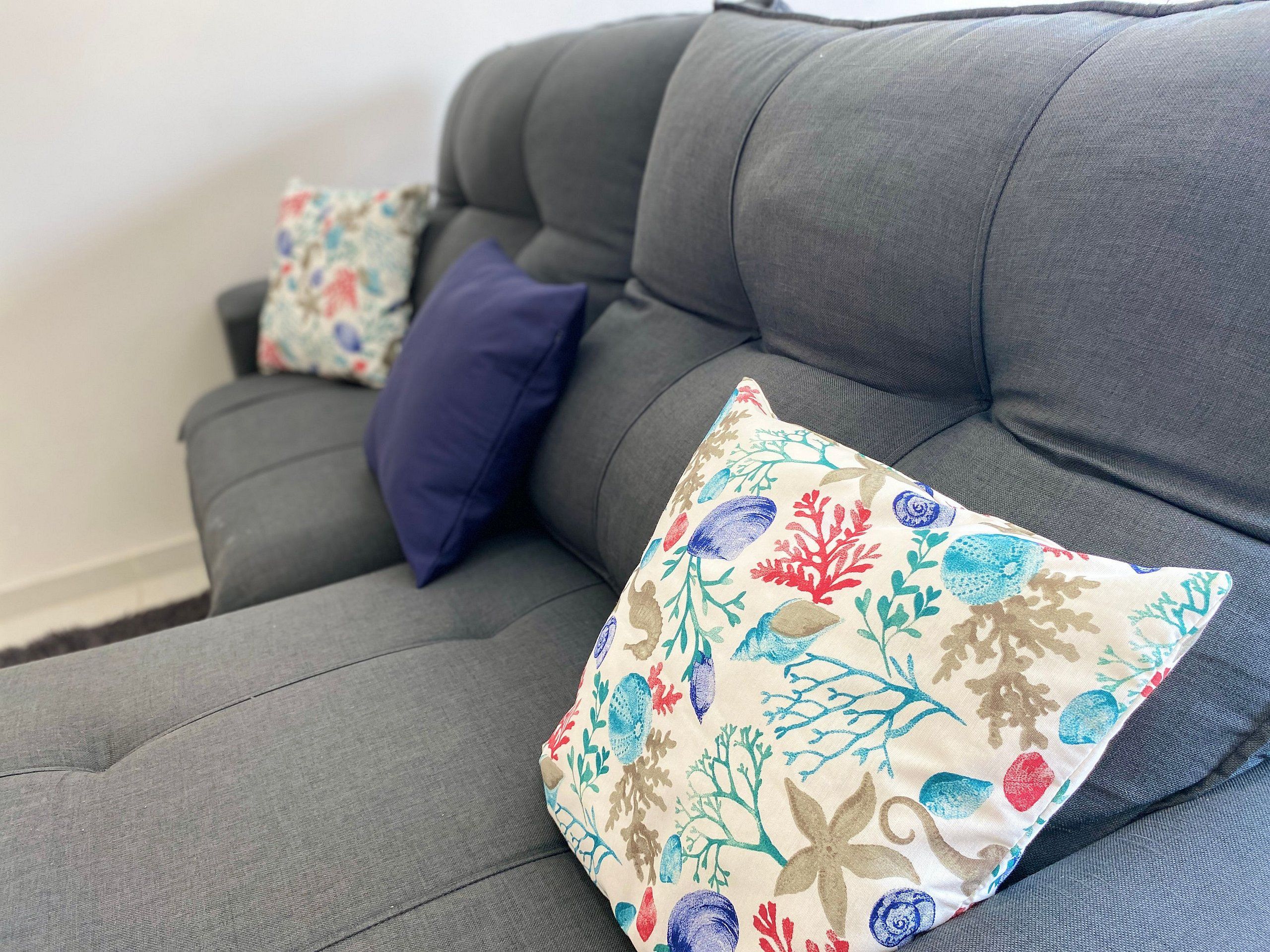 A grey sofa with two decorative pillows, one with a floral pattern and the other plain.