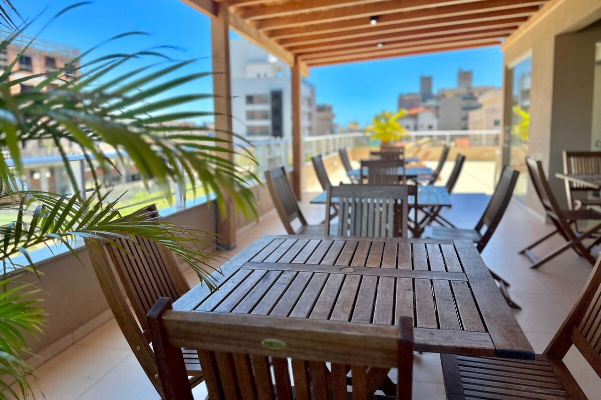 Una terraza de madera con mesas y sillas, con vista a un paisaje urbano.