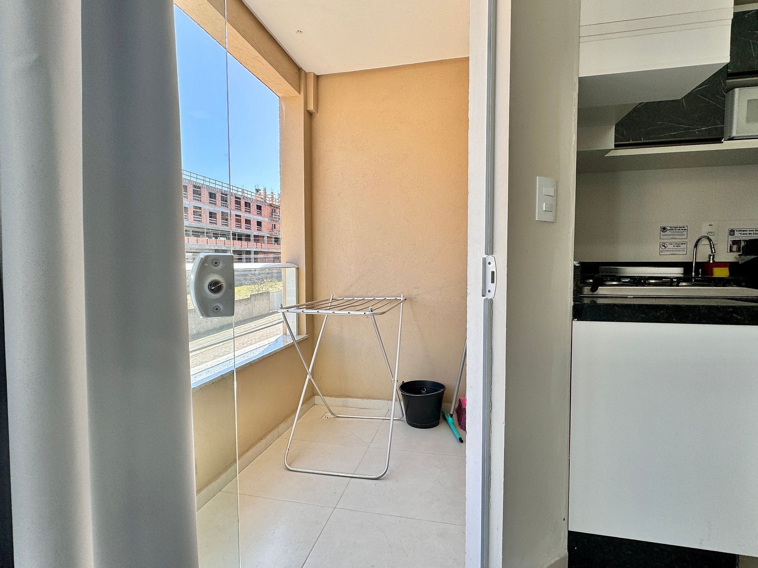 A small balcony with a drying rack, a window with a view of buildings, and a kitchen area with a sink and cabinets.