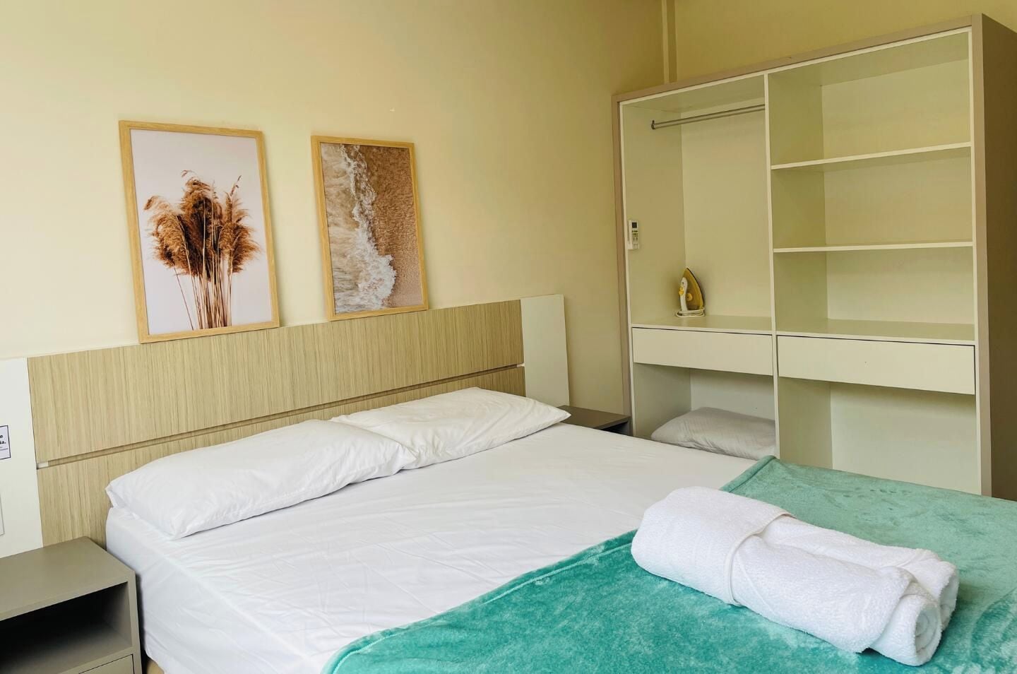 A hotel room with a bed, a nightstand, a wardrobe, and two framed pictures on the wall.