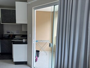 A modern kitchen with a black marble countertop, a white cabinet, and a glass door leading to a balcony. - Maria Julia (Bombinhas)