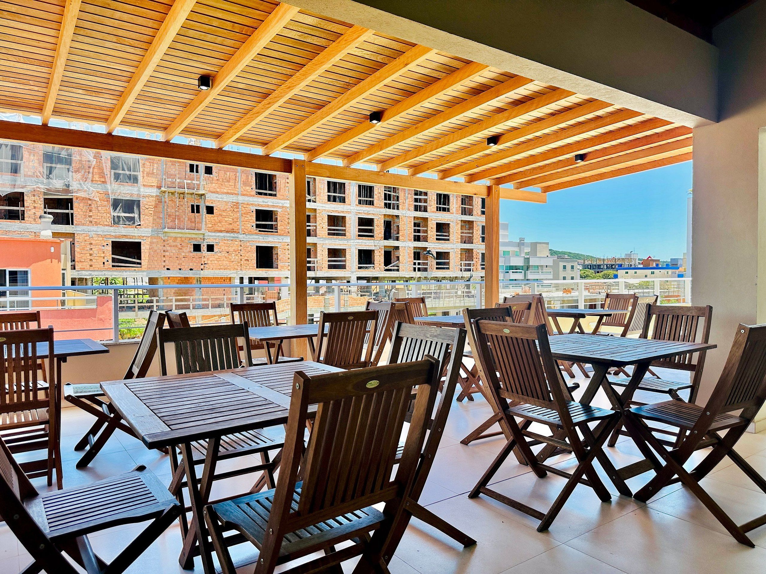 An outdoor patio with wooden tables and chairs, a wooden ceiling, and a view of a construction site in the background.