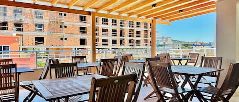 An outdoor patio with wooden tables and chairs, a wooden ceiling, and a view of a construction site in the background.