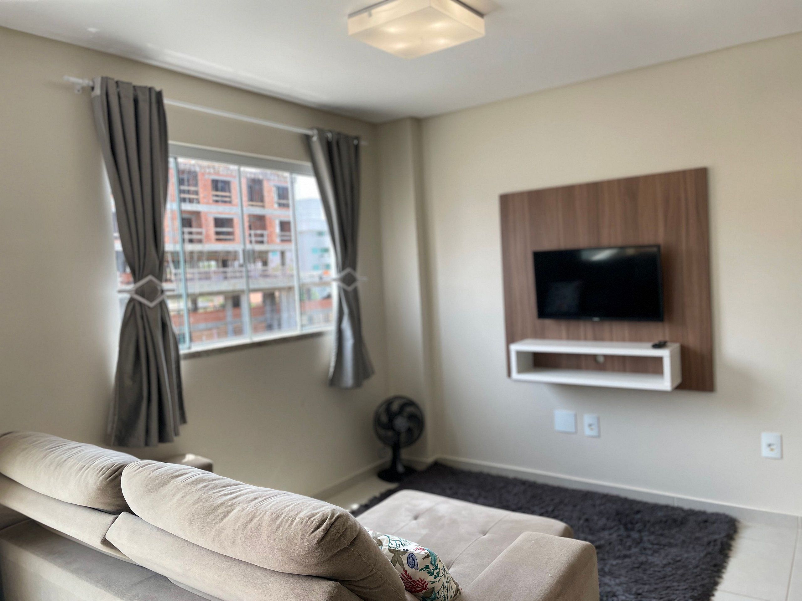 A modern living room with a sofa, a mounted TV, and a window with curtains.