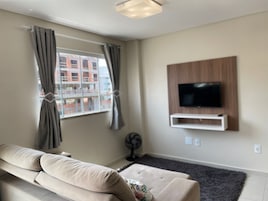 Uma sala de estar moderna com um sofá, televisão fixada na parede e uma janela com cortinas.