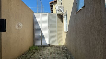 A narrow alleyway with a closed gate, a building with a textured wall, and a window with a metal grill.