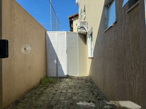 A narrow alleyway with a closed gate, a building with a textured wall, and a window with a metal grill. - Maria Julia (Bombinhas)